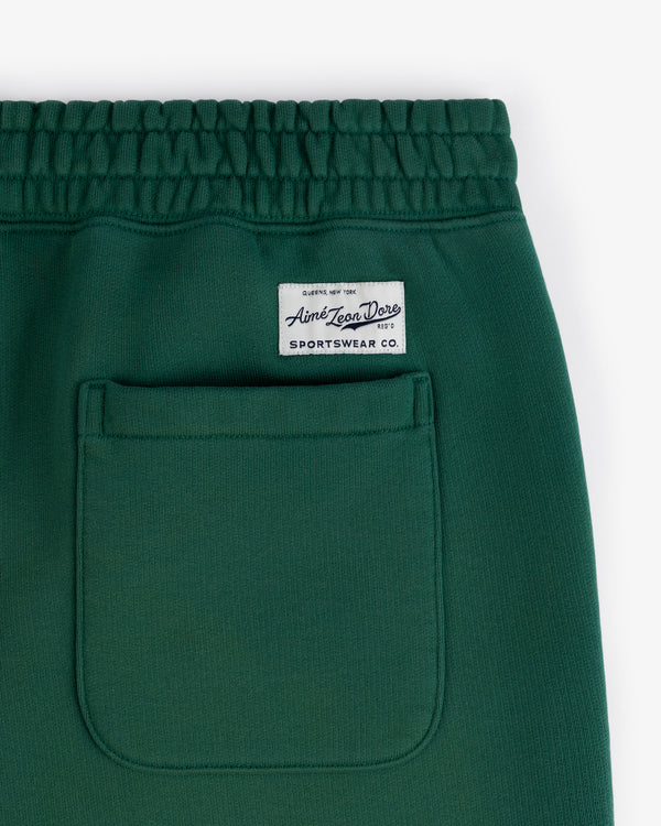 Close-up of Sun Faded Sweatpants: green with elastic waistband, back pocket, and white Aimé Leon Dore label above.
