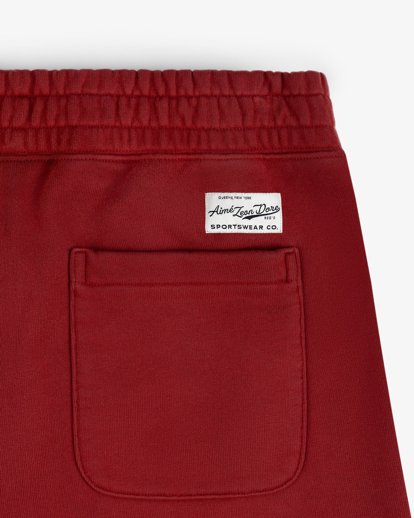 Close-up of Sun Faded Sweatpants in red with an elastic waistband, back pocket, and white sportswear label.