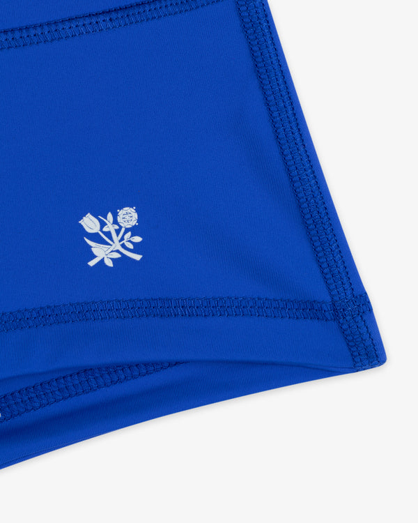 Close-up of Crest Swim Short's blue fabric with dark stitching and a small white floral logo.