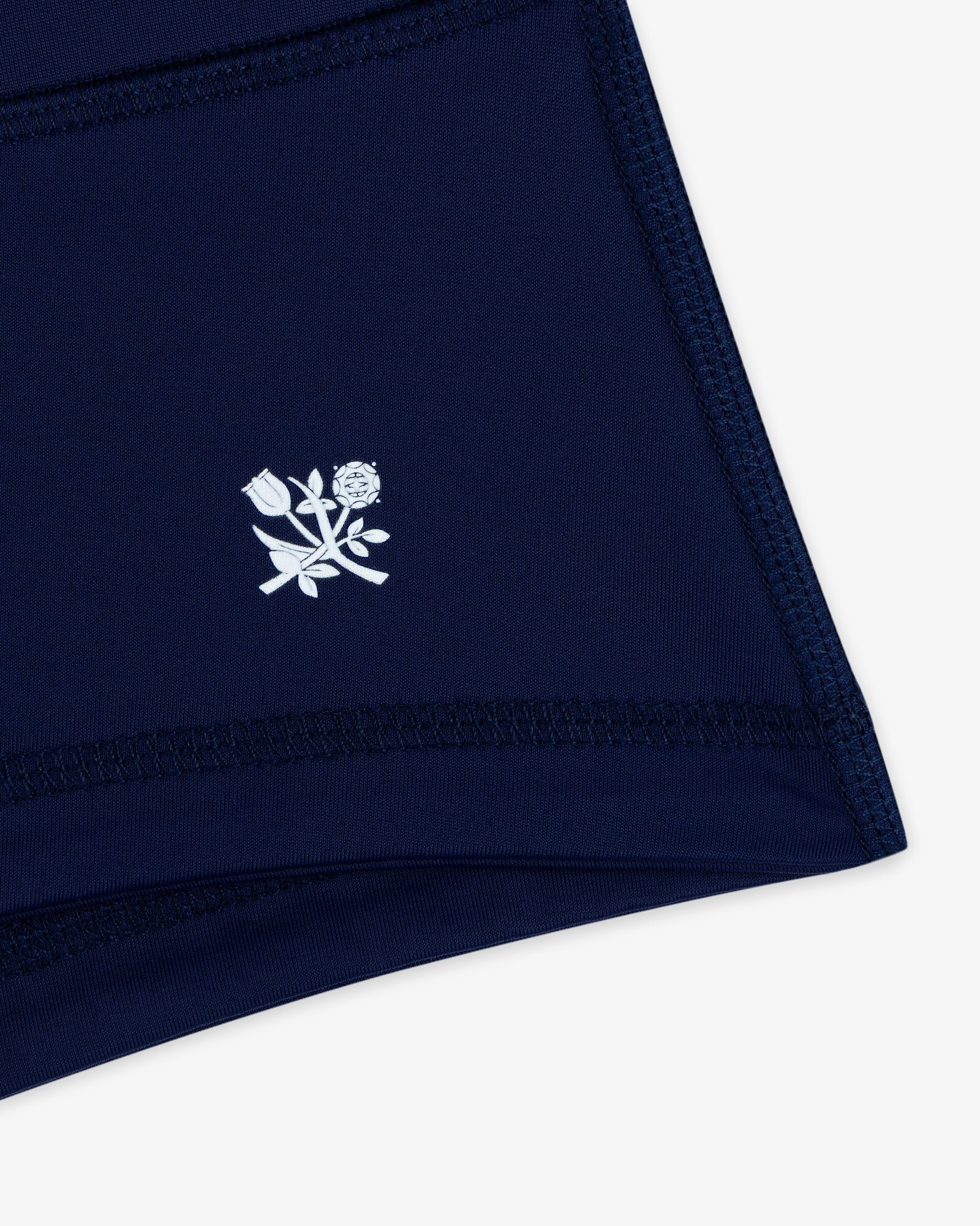 Crest Swim Short in navy blue fabric with white stitched outline and a small white floral graphic near the hem.