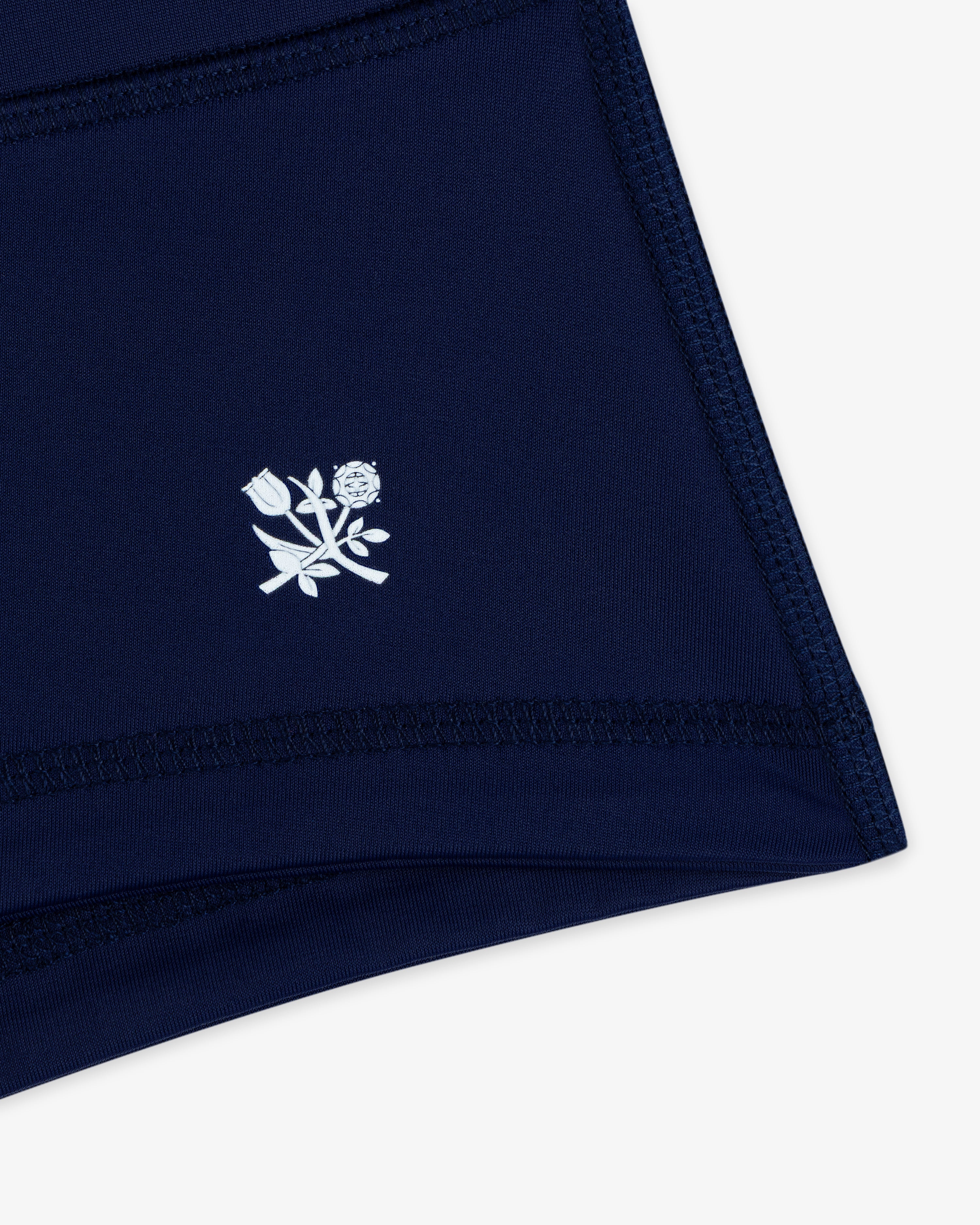 Crest Swim Short in navy blue fabric with white stitched outline and a small white floral graphic near the hem.