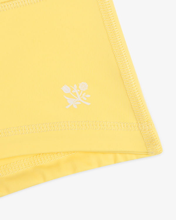Close-up of Crest Swim Short's yellow fabric with visible stitching and a small white floral graphic.