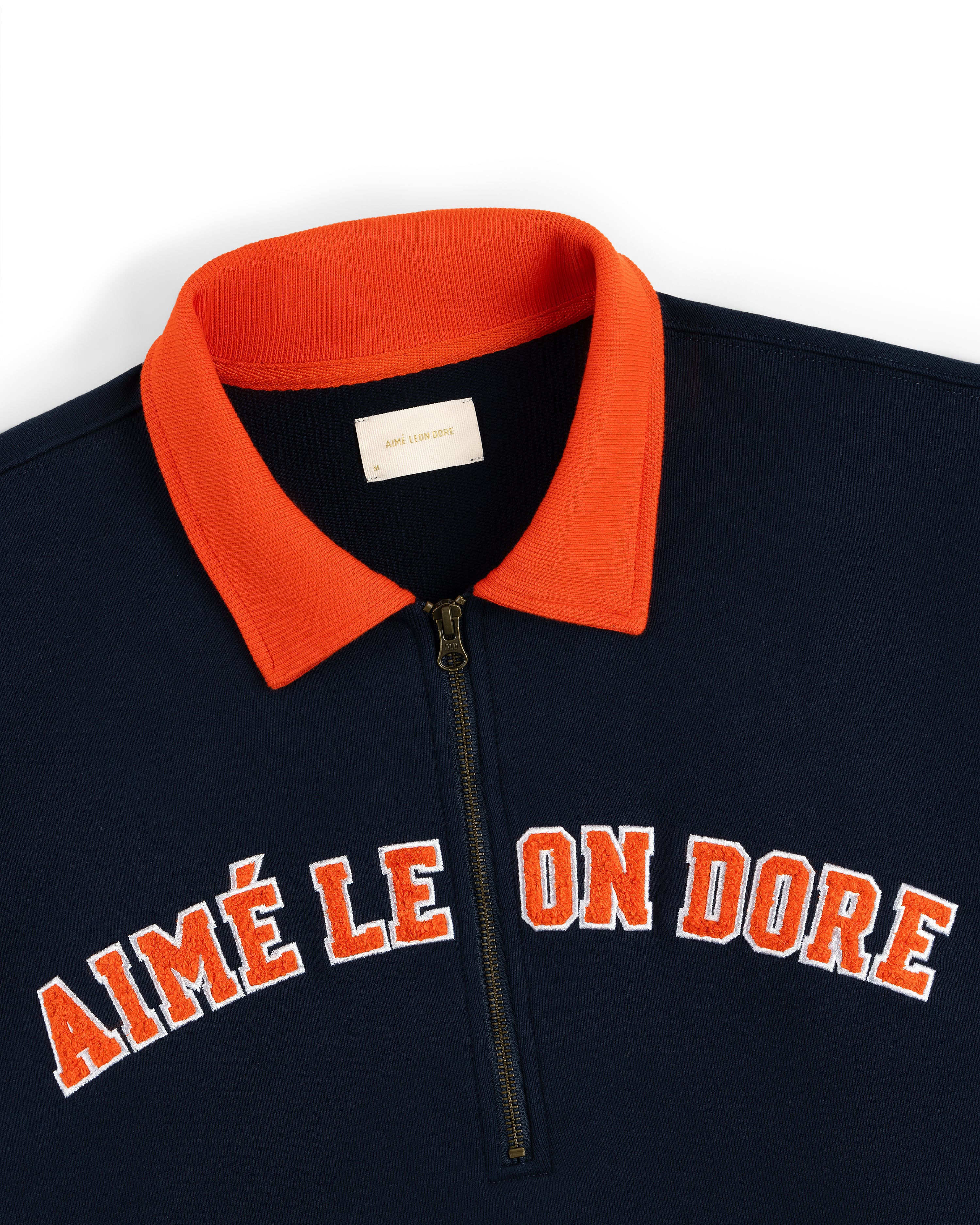 Collegiate Quarter Zip Pullover: Navy shirt with AIMÉ LEON DORE in red/white and an orange collar.