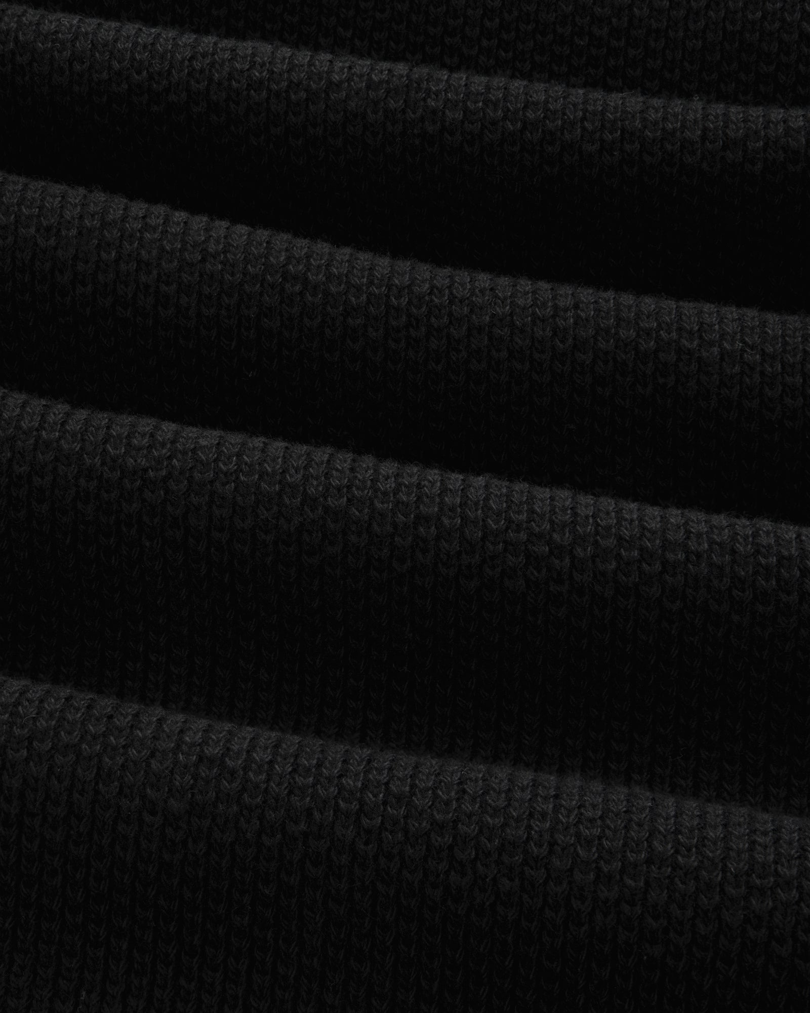 Close-up of the ALD Golf Piqué Full Zip Sweater's folded black ribbed fabric with visible textured lines.
