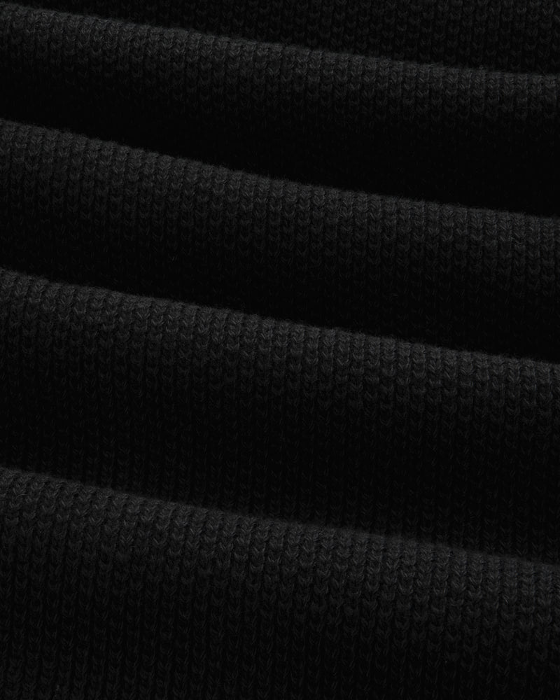 Close-up of the ALD Golf Piqué Full Zip Sweater's folded black ribbed fabric with visible textured lines.