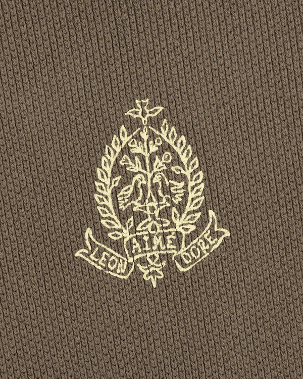 Cream embroidered crest with floral and leaf patterns, LEON AIME COPE text on brown Saint George Piqué Crewneck Sweatshirt.