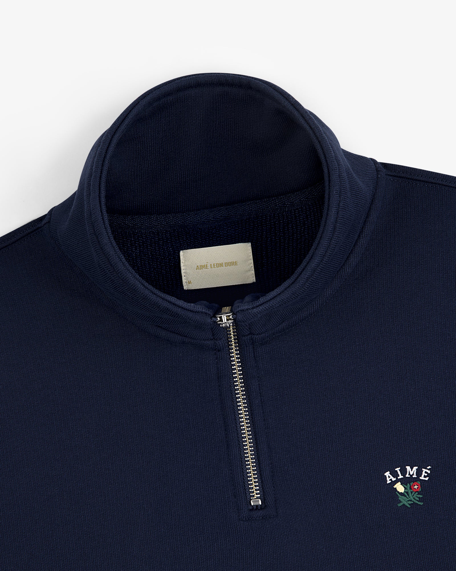 Navy Crest Quarter Zip Pullover with AIMÉ and a rose embroidered on chest, plus a visible label inside the collar.