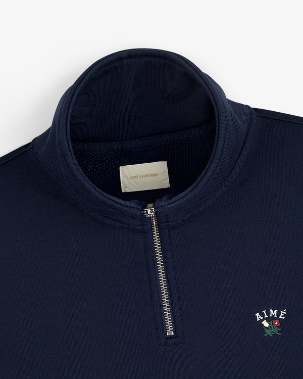 Navy Crest Quarter Zip Pullover with AIMÉ and a rose embroidered on chest, plus a visible label inside the collar.