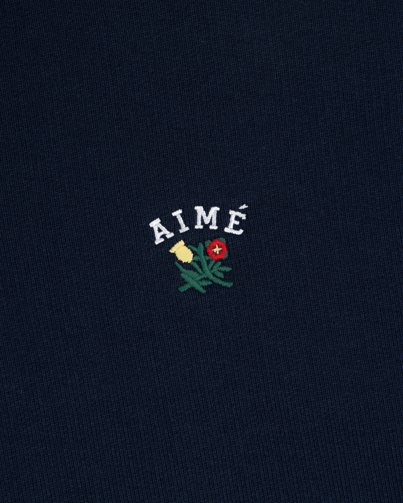 Navy Crest Quarter Zip Pullover with AIMÉ embroidered above a green plant with yellow and red flowers.