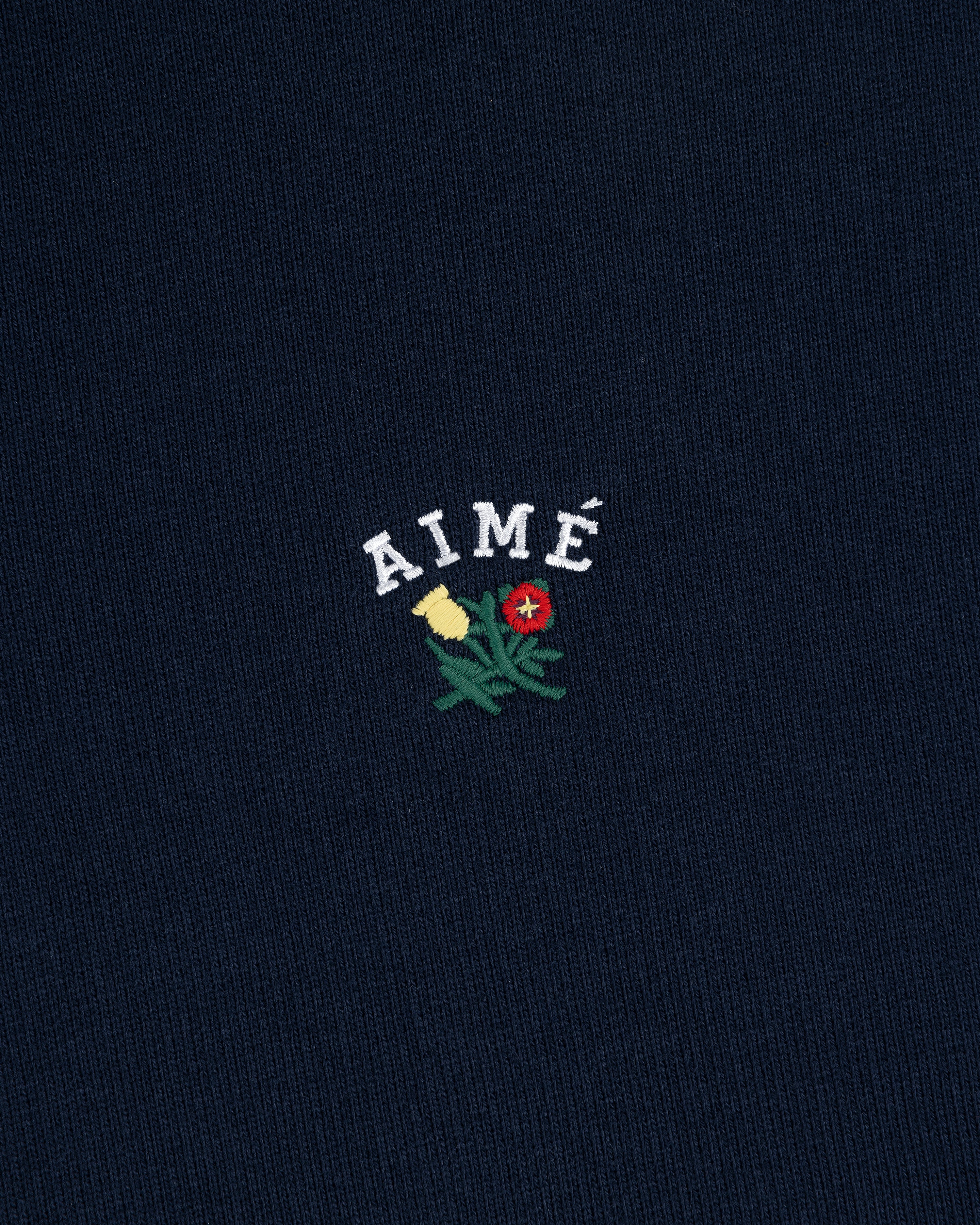 Navy Crest Quarter Zip Pullover with AIMÉ embroidered above a green plant with yellow and red flowers.