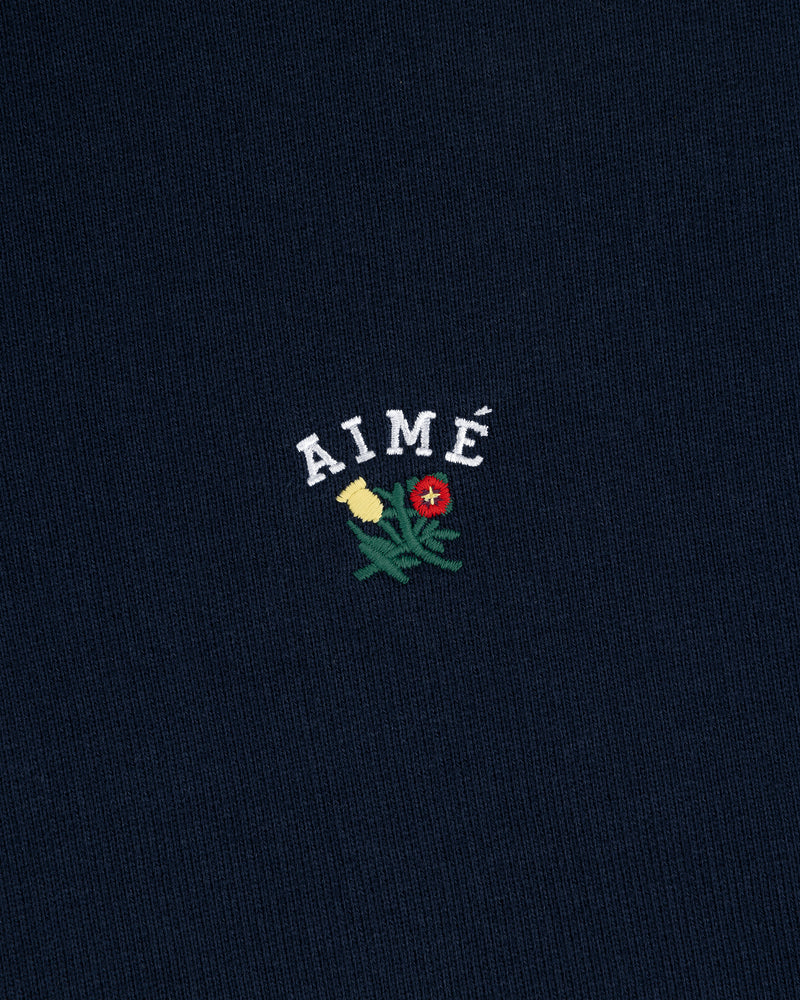Navy Crest Quarter Zip Pullover with AIMÉ embroidered above a green plant with yellow and red flowers.
