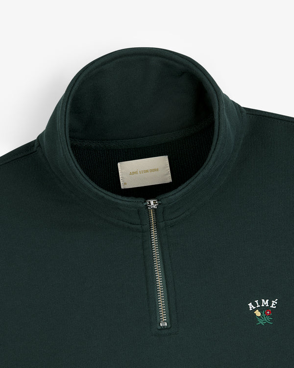 Dark green Crest Quarter Zip Pullover featuring AIMÉ and a rose embroidered on the left chest.