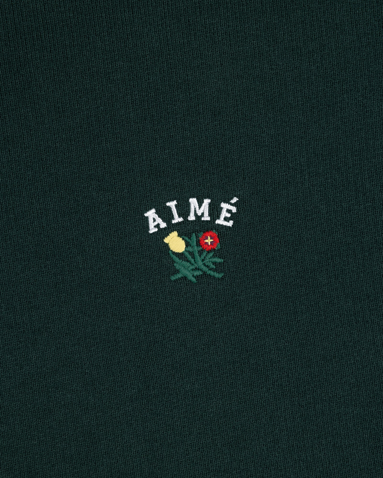 Dark green Crest Quarter Zip Pullover with AIMÉ embroidered above a yellow and red flower with green leaves.
