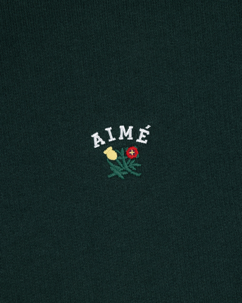 Dark green Crest Quarter Zip Pullover with AIMÉ embroidered above a yellow and red flower with green leaves.