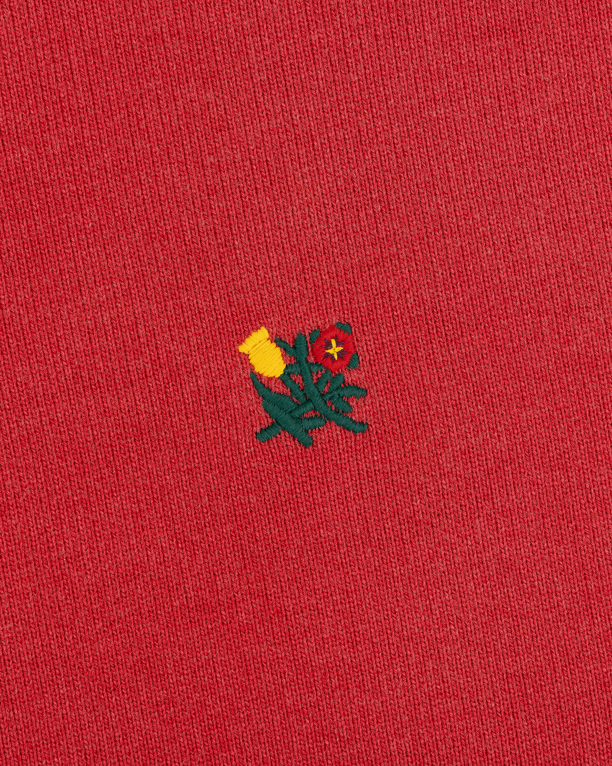 Close-up of red Sun Faded Crest Quarter Zip featuring a small embroidered yellow and red flower in the center.