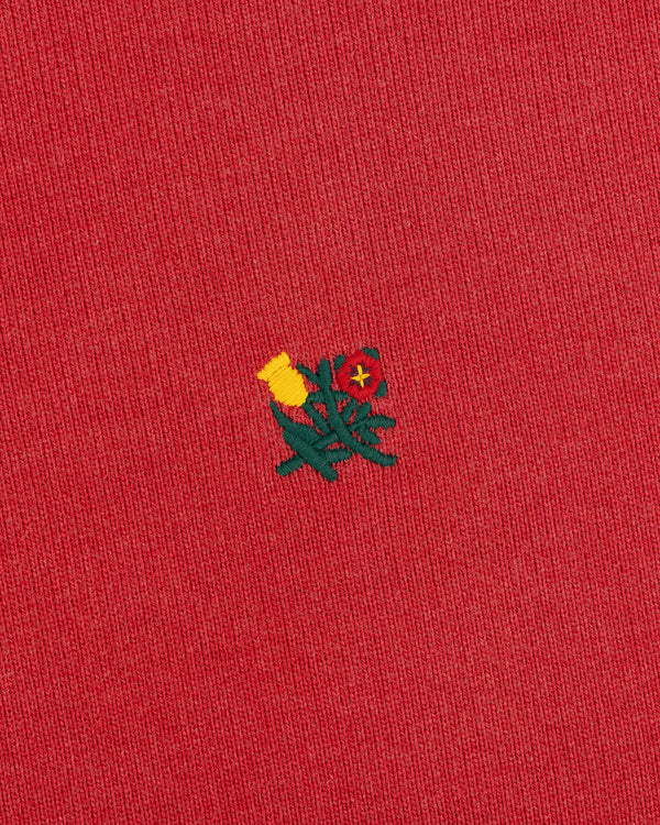 Close-up of red Sun Faded Crest Quarter Zip featuring a small embroidered yellow and red flower in the center.