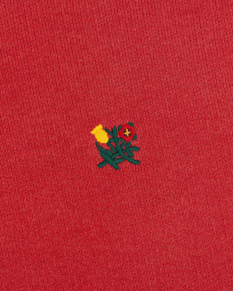 Close-up of red Sun Faded Crest Quarter Zip featuring a small embroidered yellow and red flower in the center.