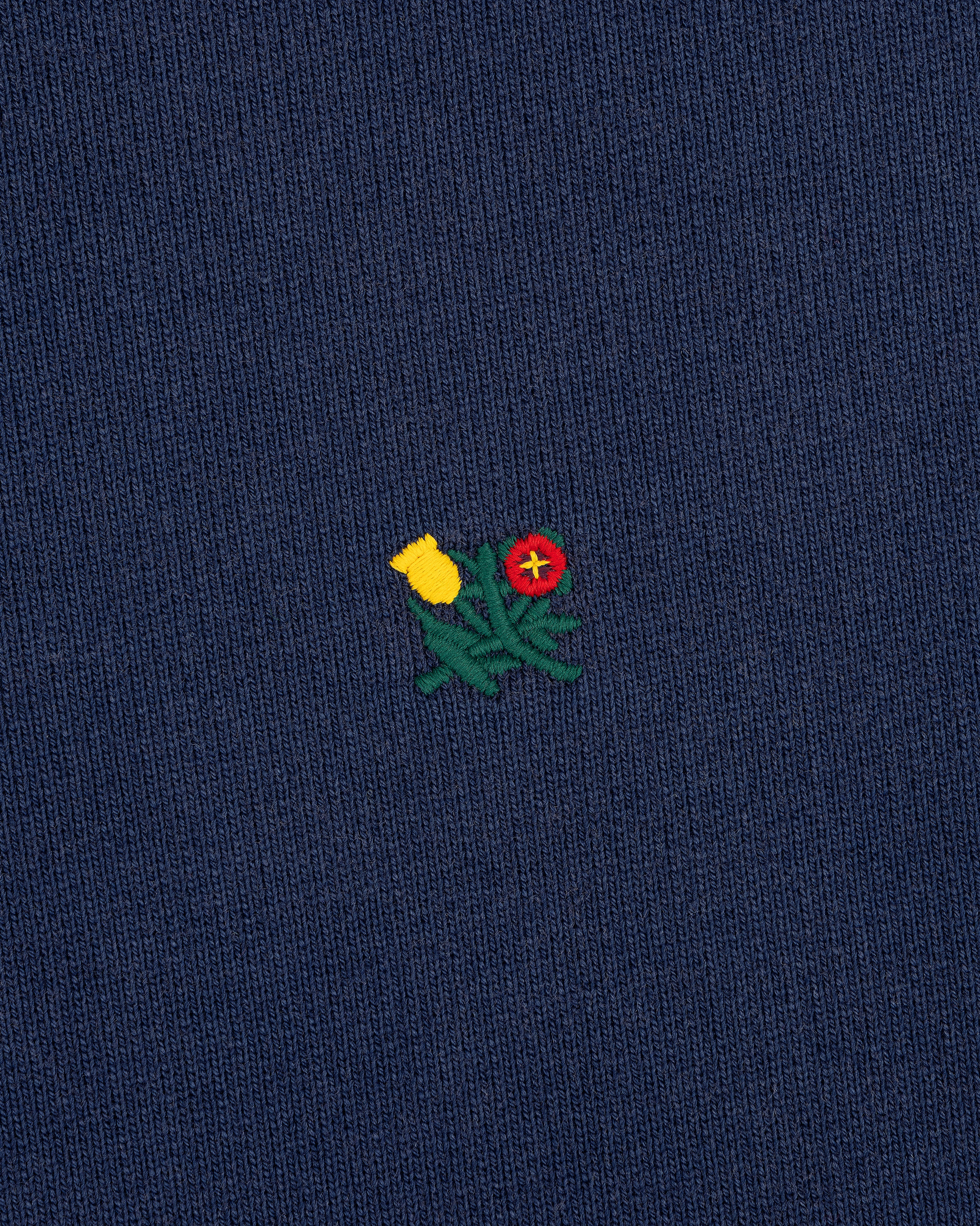 Small embroidered yellow and red flowers on dark blue Sun Faded Crest Quarter Zip with green stems.