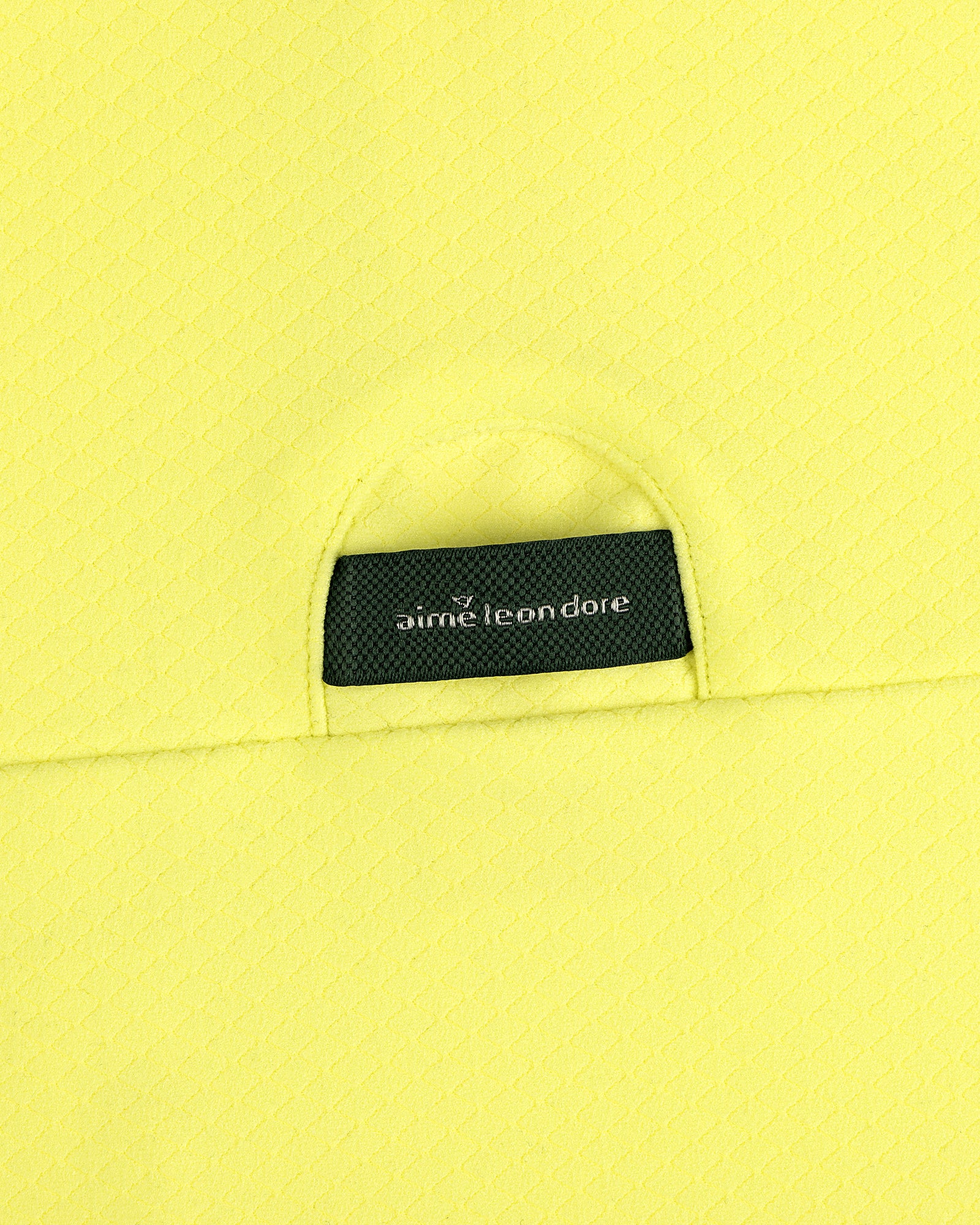 A close-up of an ALD Golf Quarter Zip Pullover’s black Aimé Leon Dore label sewn onto textured yellow fabric.