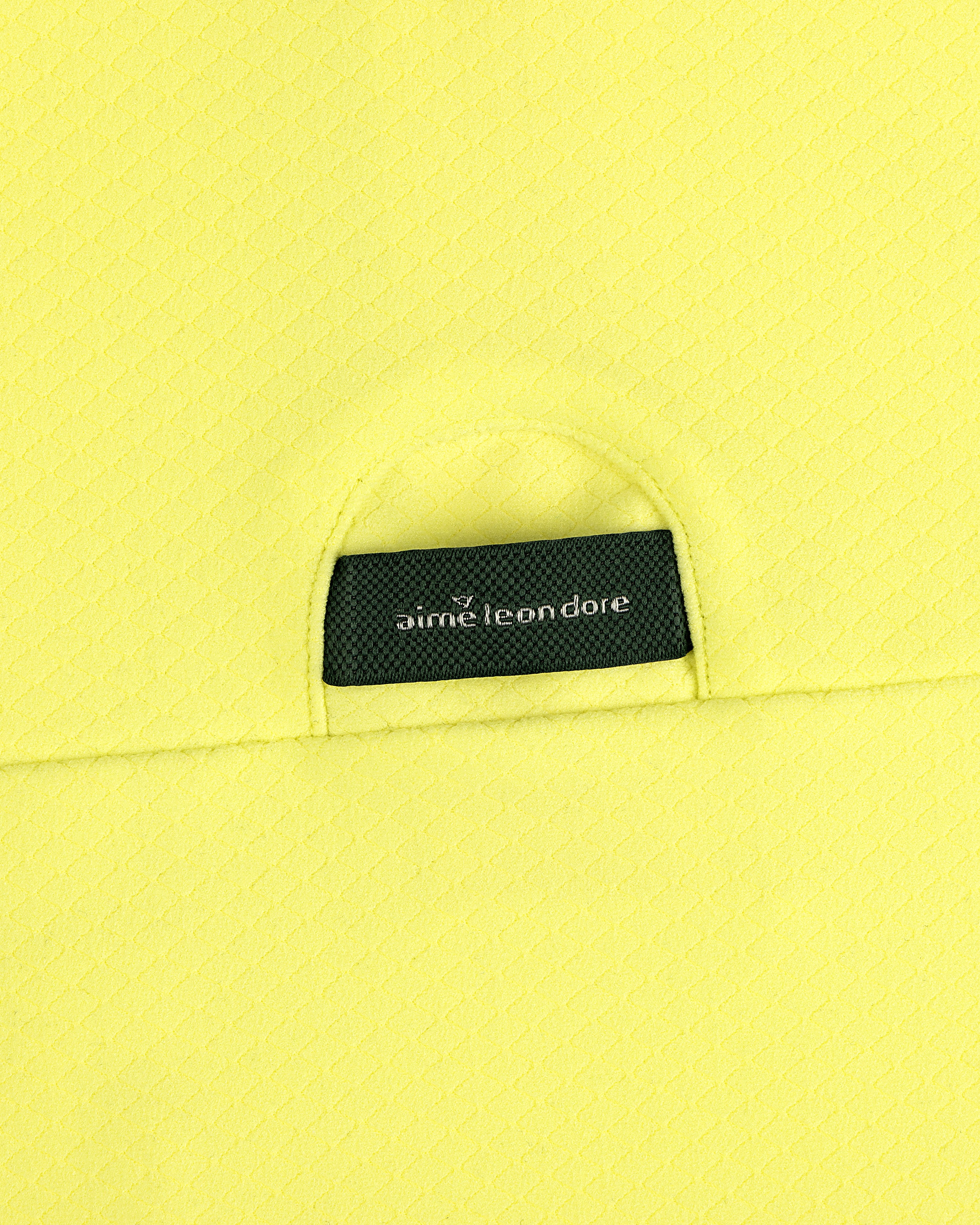 A close-up of an ALD Golf Quarter Zip Pullover’s black Aimé Leon Dore label sewn onto textured yellow fabric.