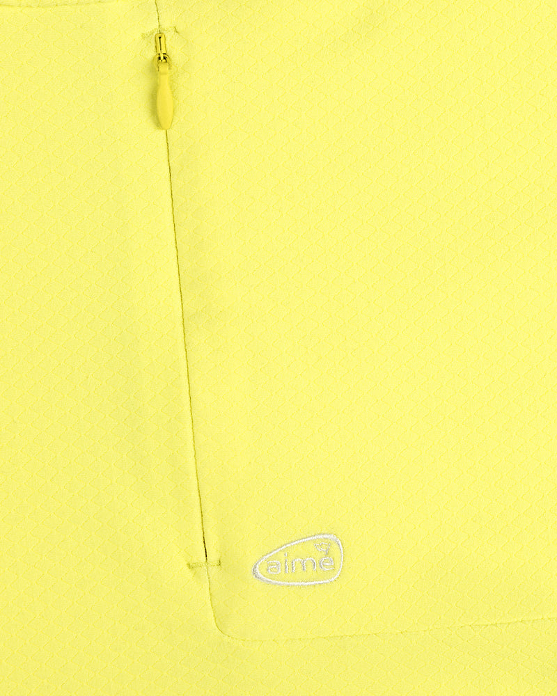 Close-up of ALD Golf Quarter Zip Pullover in yellow with textured fabric, zip pocket, and embroidered white aimé logo.