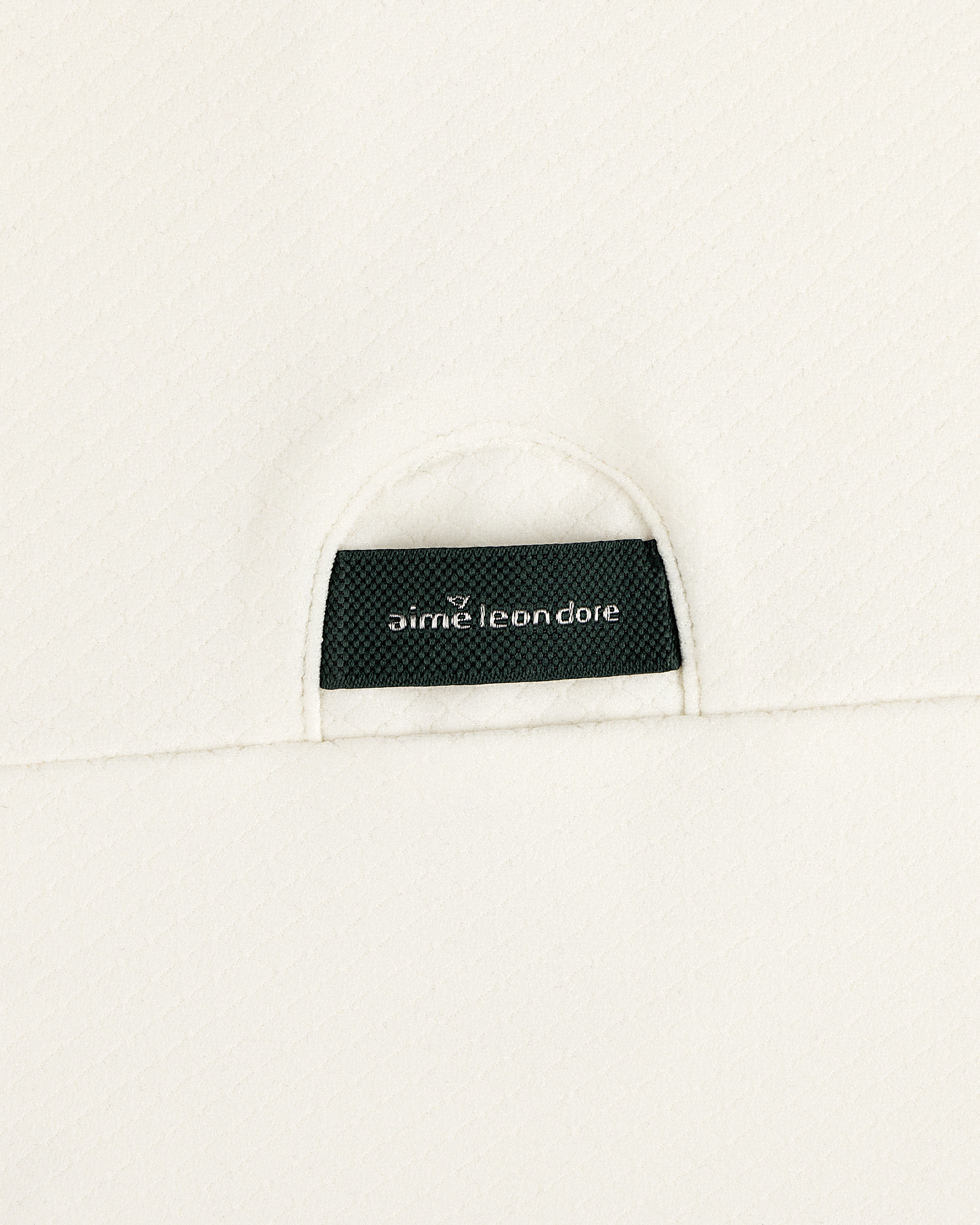 A black Aimé Leon Dore label sewn into the off-white ALD Golf Quarter Zip Pullover’s textured fabric.