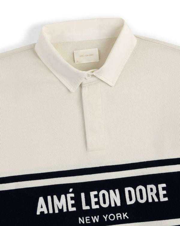 Chest Stripe Logo Rugby with a cream base, collar, and AIMÉ LEON DORE NEW YORK text on a navy chest stripe.