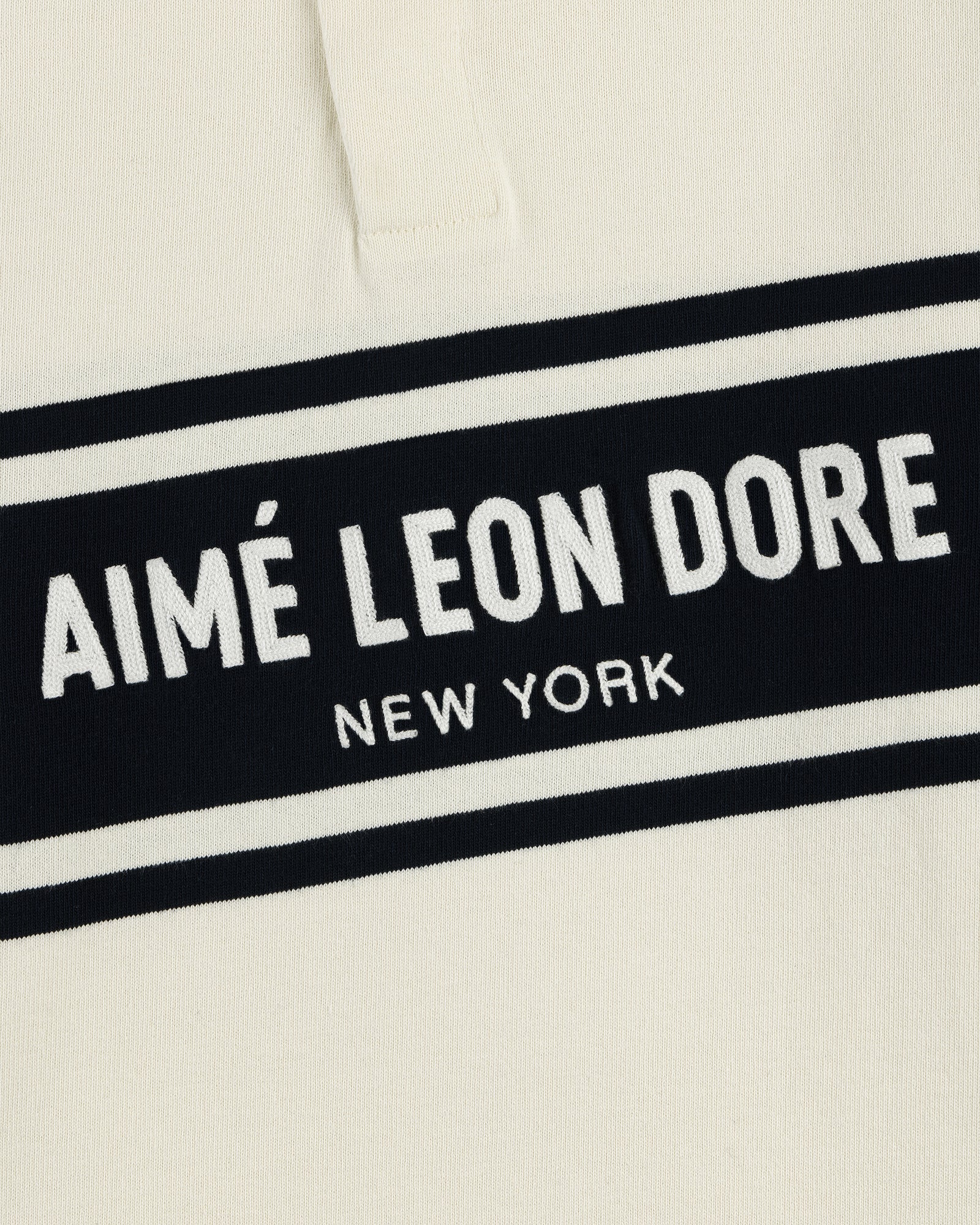 Close-up of the Chest Stripe Logo Rugby in cream with AIMÉ LEON DORE NEW YORK in white on a black chest stripe.