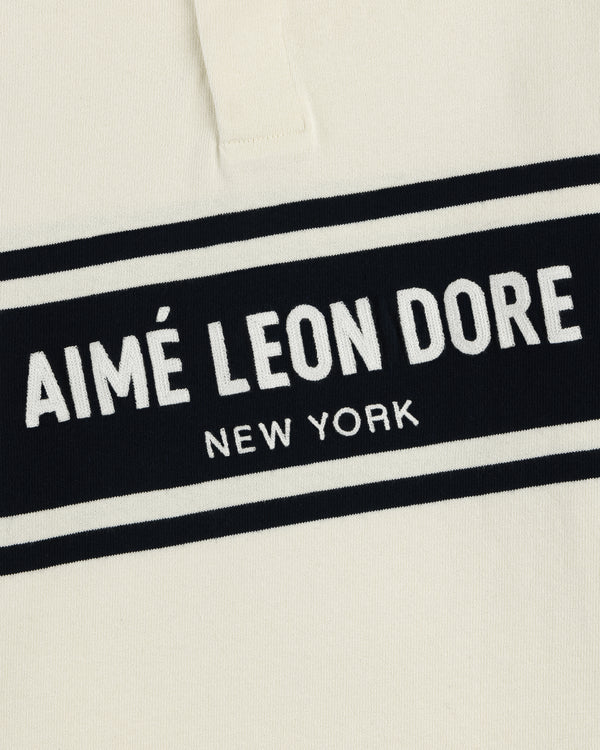 Close-up of the Chest Stripe Logo Rugby in cream with AIMÉ LEON DORE NEW YORK in white on a black chest stripe.