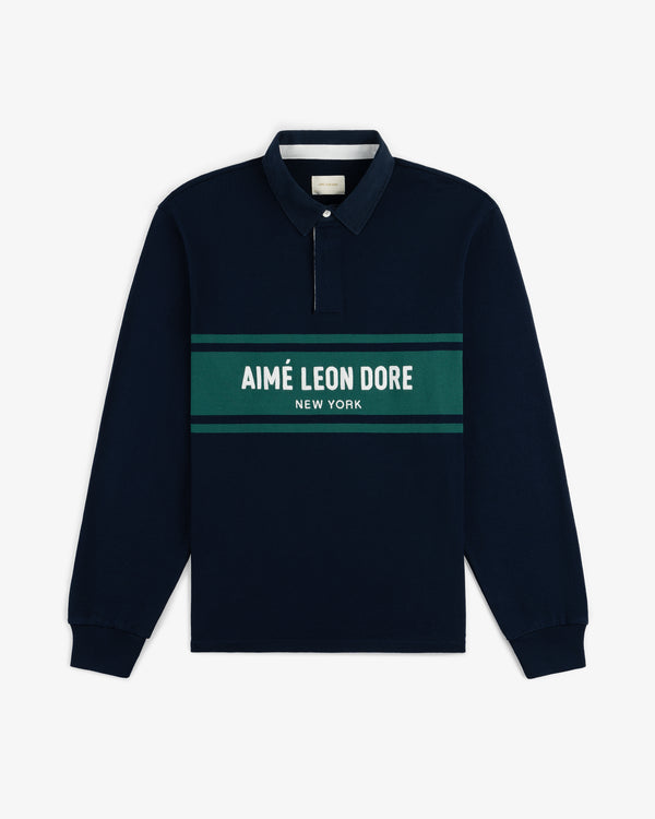 Chest Stripe Logo Rugby in navy with green and white stripes and “AIMÉ LEON DORE NEW YORK” across the chest.