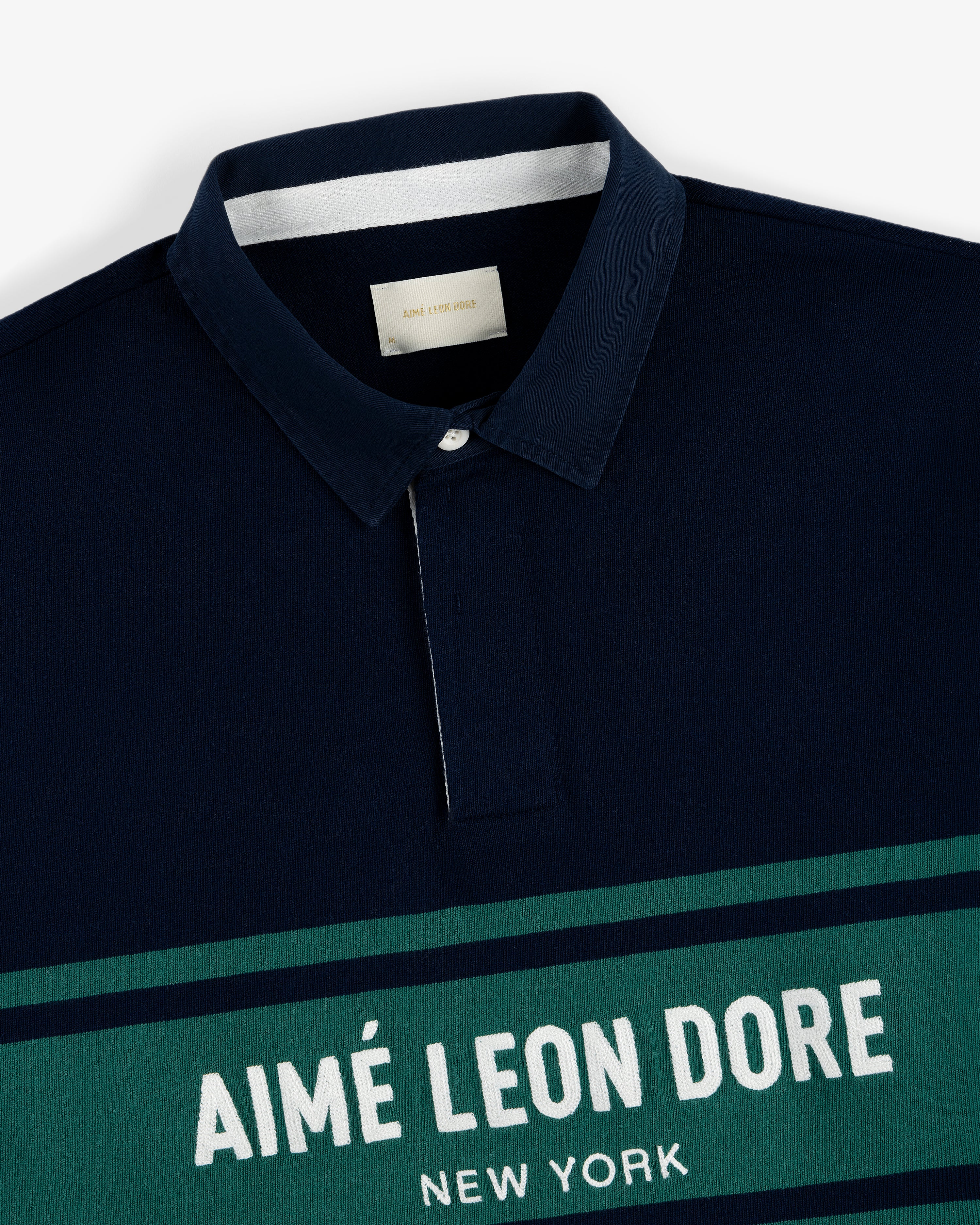 Navy Chest Stripe Logo Rugby with green and white stripes and AIMÉ LEON DORE NEW YORK printed on the front.