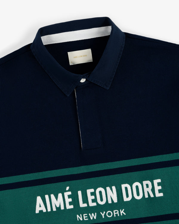 Navy Chest Stripe Logo Rugby with green and white stripes and AIMÉ LEON DORE NEW YORK printed on the front.