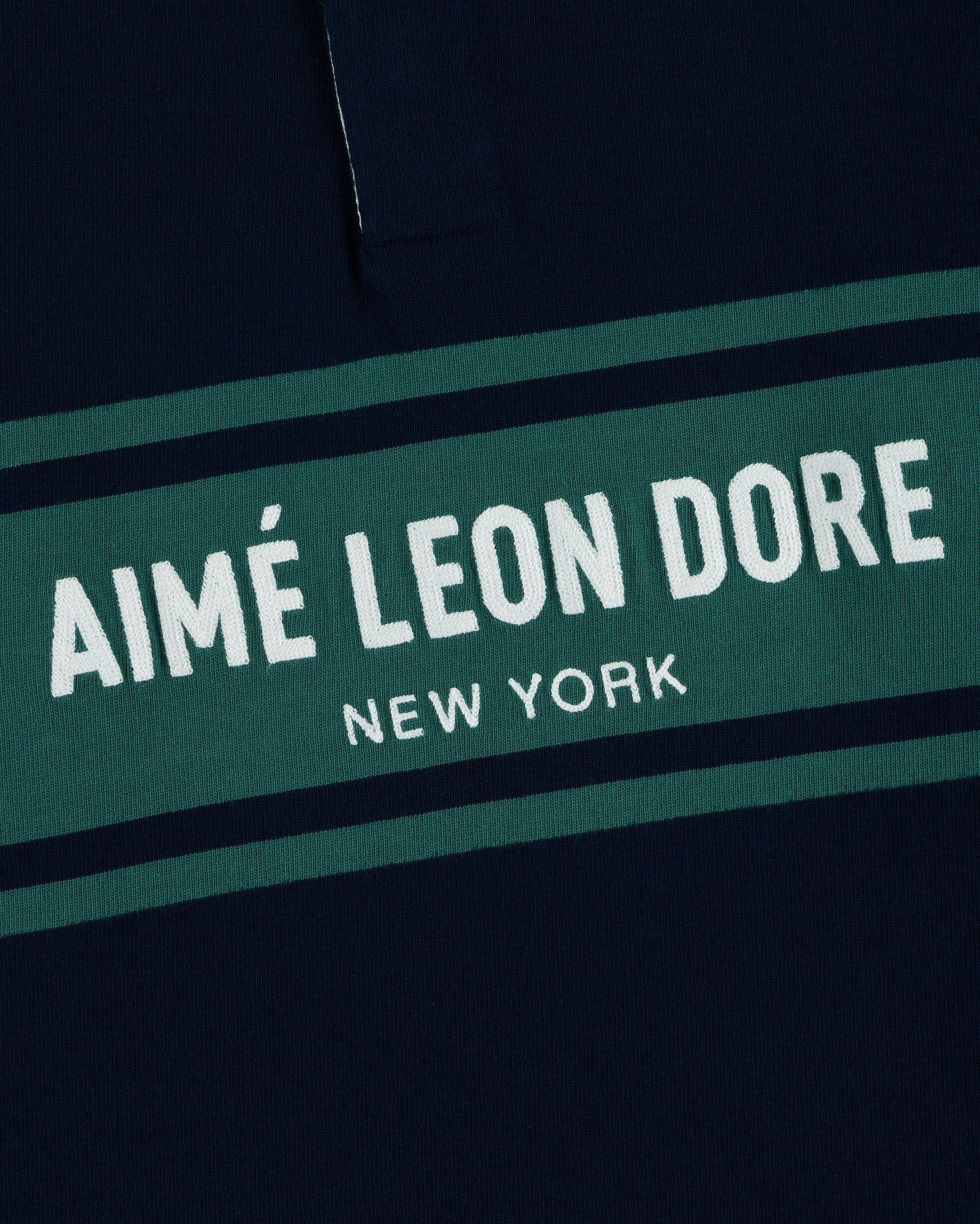 Close-up of the Chest Stripe Logo Rugby with AIMÉ LEON DORE NEW YORK in white on a green stripe.