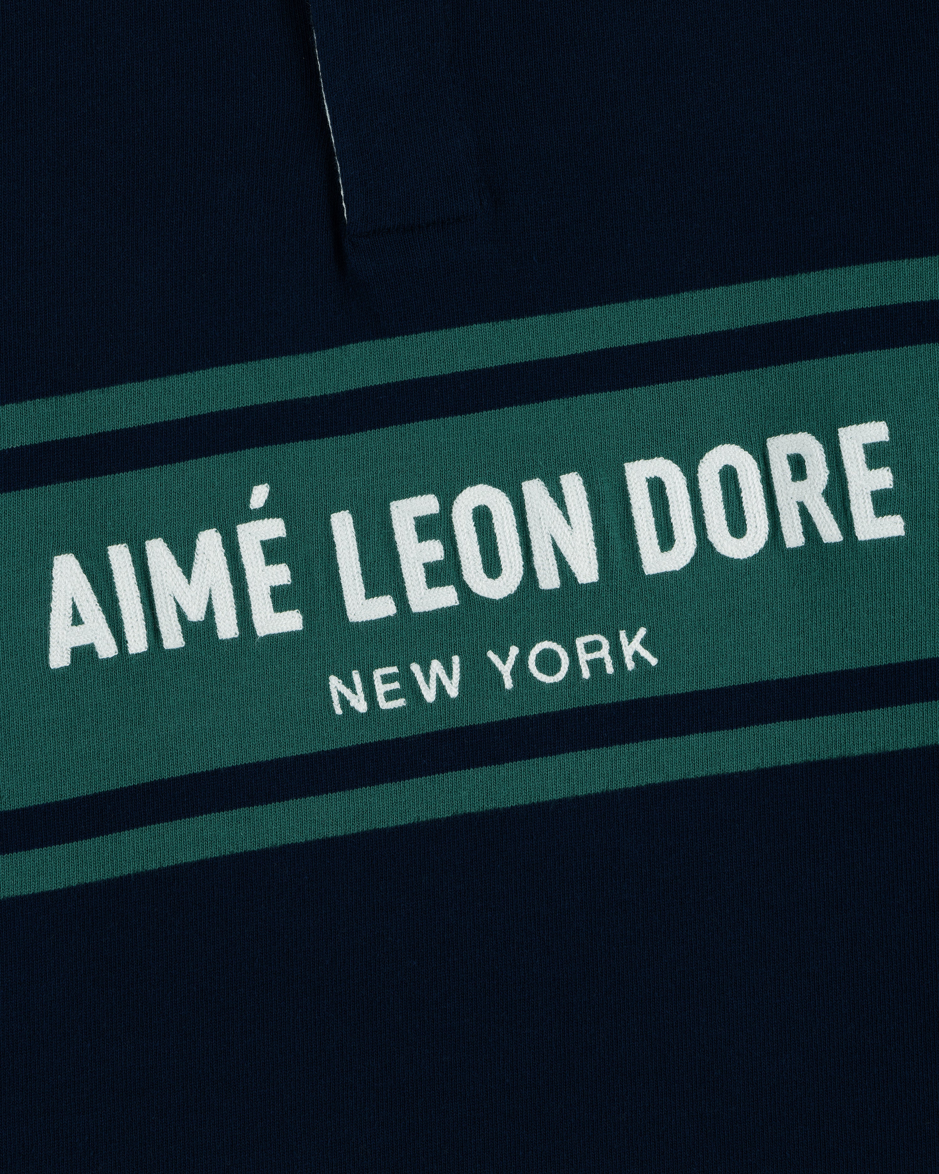 Close-up of the Chest Stripe Logo Rugby with AIMÉ LEON DORE NEW YORK in white on a green stripe.