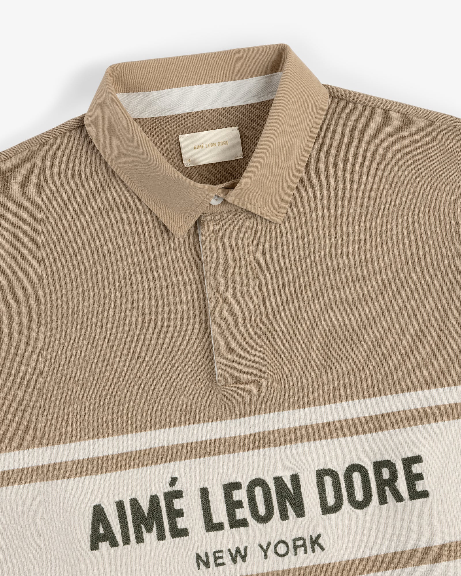 Beige Chest Stripe Logo Rugby with a collar and AIMÉ LEON DORE NEW YORK text on the front.