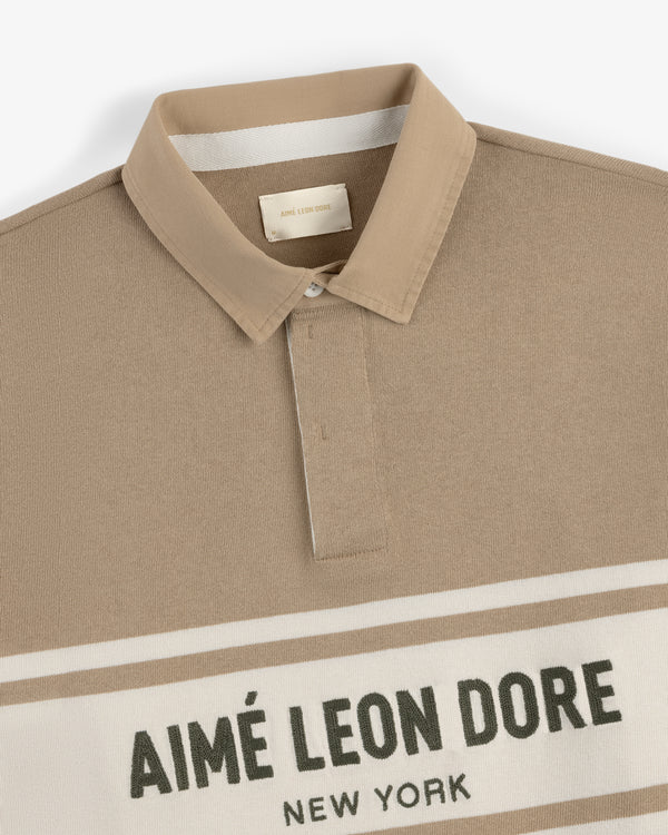 Beige Chest Stripe Logo Rugby with a collar and AIMÉ LEON DORE NEW YORK text on the front.