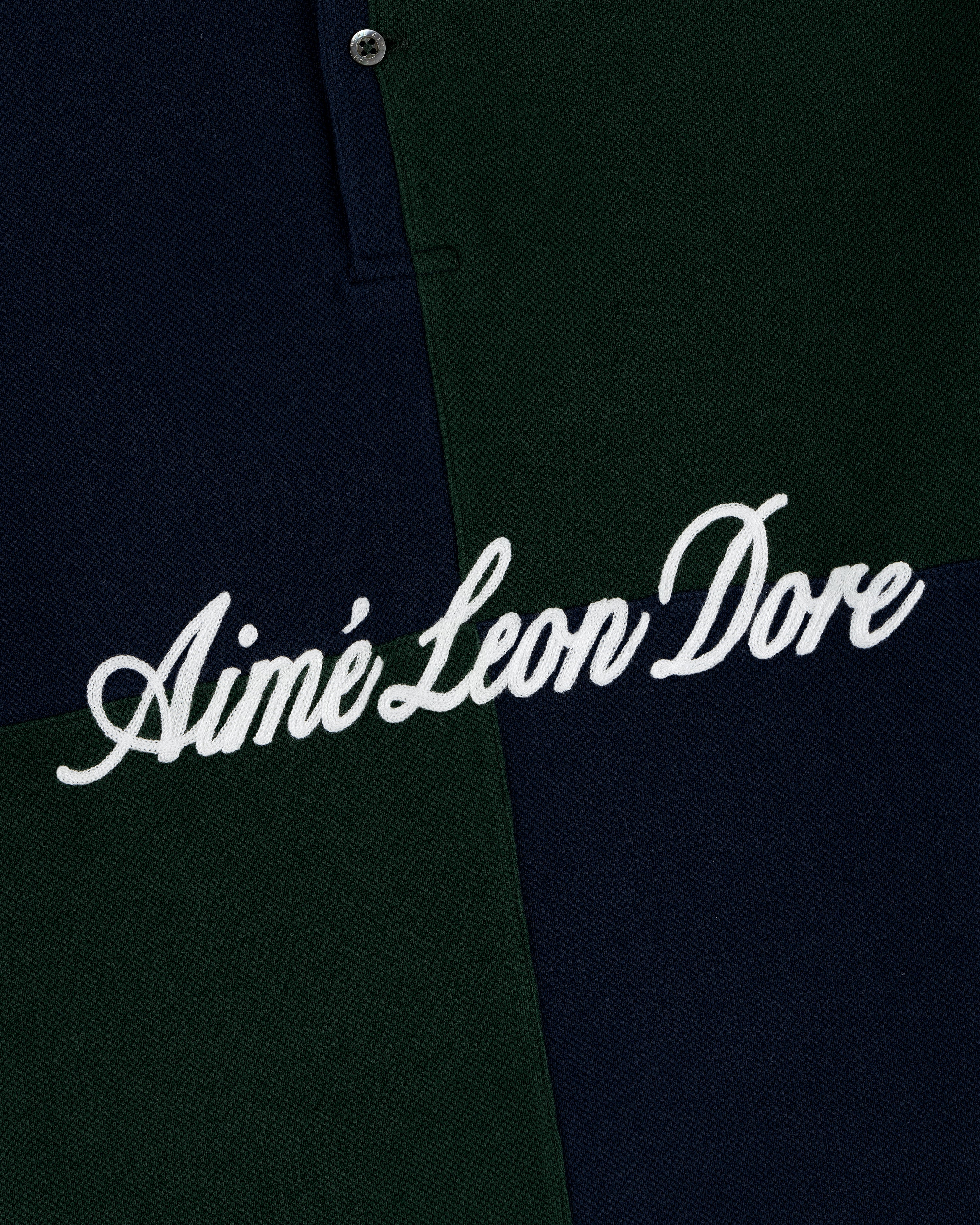 Close-up of a dark green and navy Color Blocked Pique Polo with Aimé Leon Dore embroidered in white cursive text.