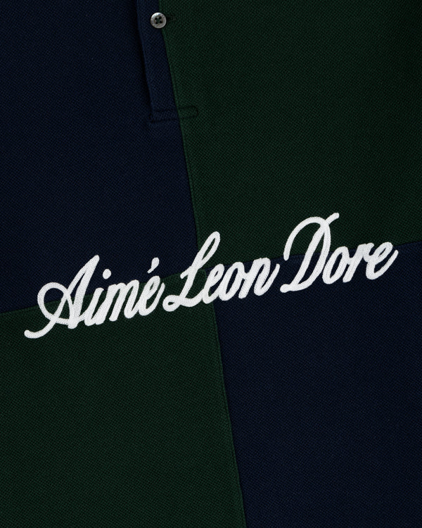 Close-up of a dark green and navy Color Blocked Pique Polo with Aimé Leon Dore embroidered in white cursive text.