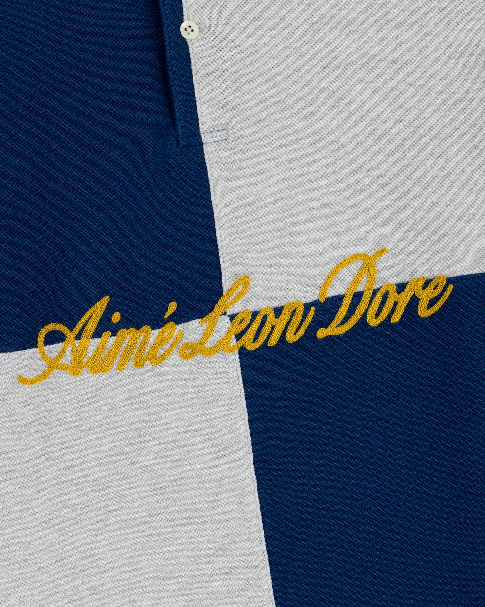 Close-up of the Color Blocked Pique Polo's blue and gray checkered fabric with yellow Aimé Leon Dore embroidery.