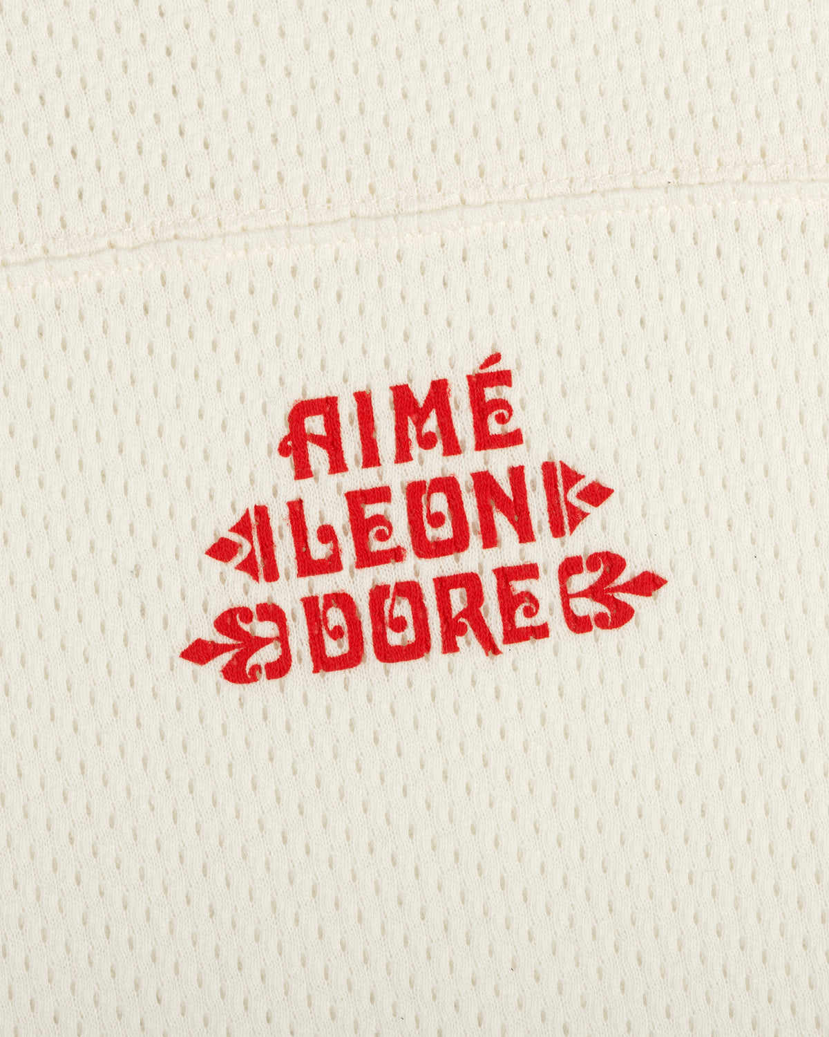 Cream perforated Pointelle Stacked Logo Tee with bold red AIMÉ LEON DORE text in a vintage-inspired font.