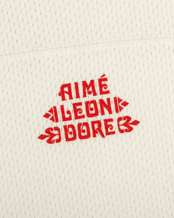 Cream perforated Pointelle Stacked Logo Tee with bold red AIMÉ LEON DORE text in a vintage-inspired font.
