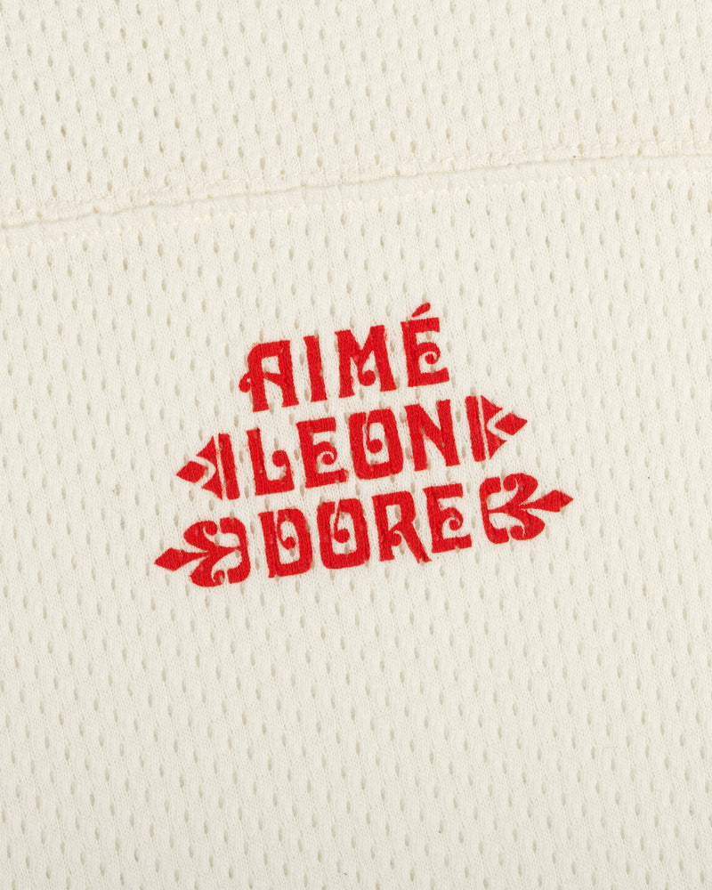 Cream perforated Pointelle Stacked Logo Tee with bold red AIMÉ LEON DORE text in a vintage-inspired font.