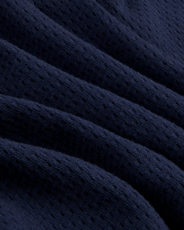 Close-up of dark blue, textured Pointelle Stacked Logo Tee with perforated fabric and wavy folds.