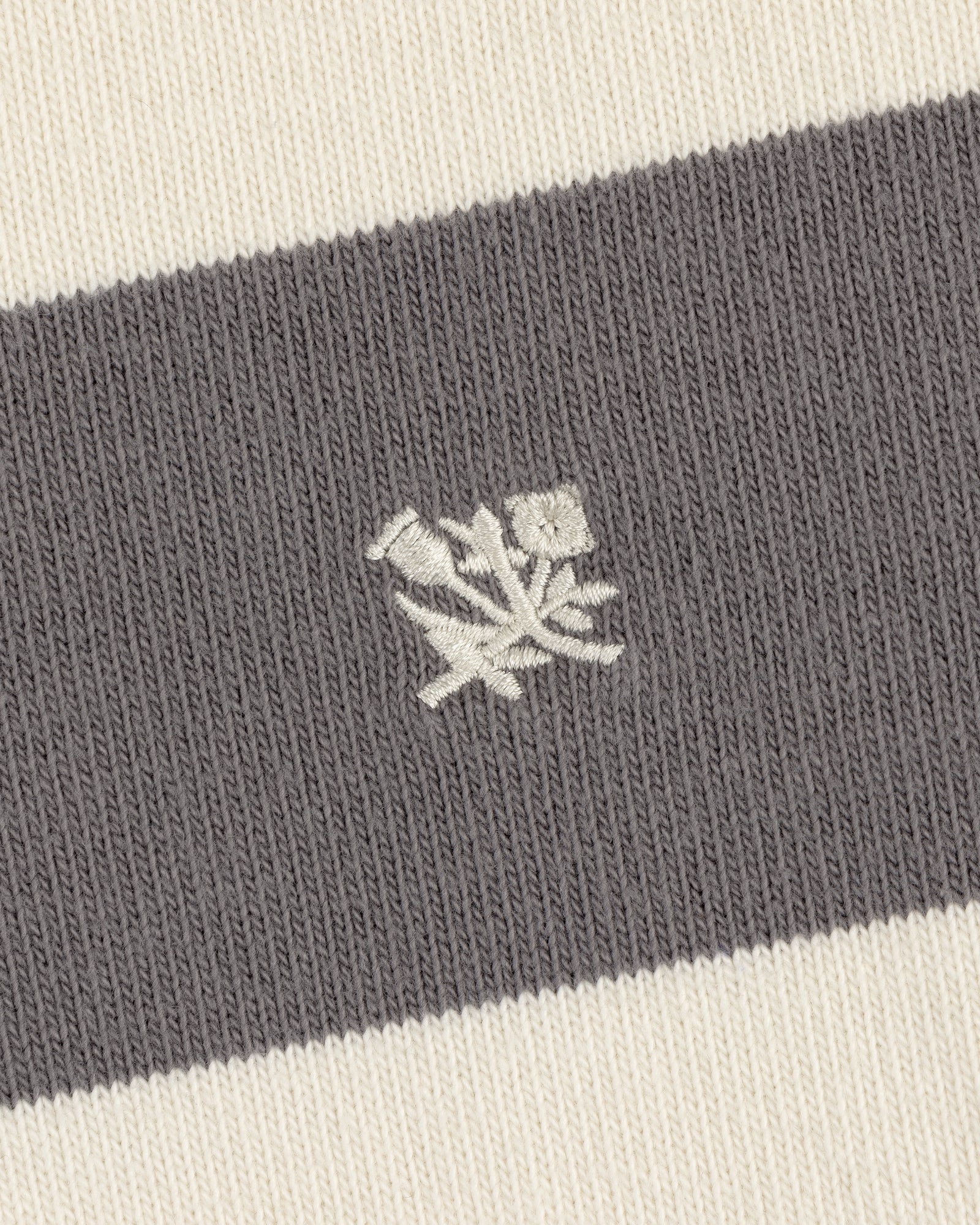 Close-up of the Striped Crest Rugby's gray and white knit fabric with an embroidered white rose emblem.