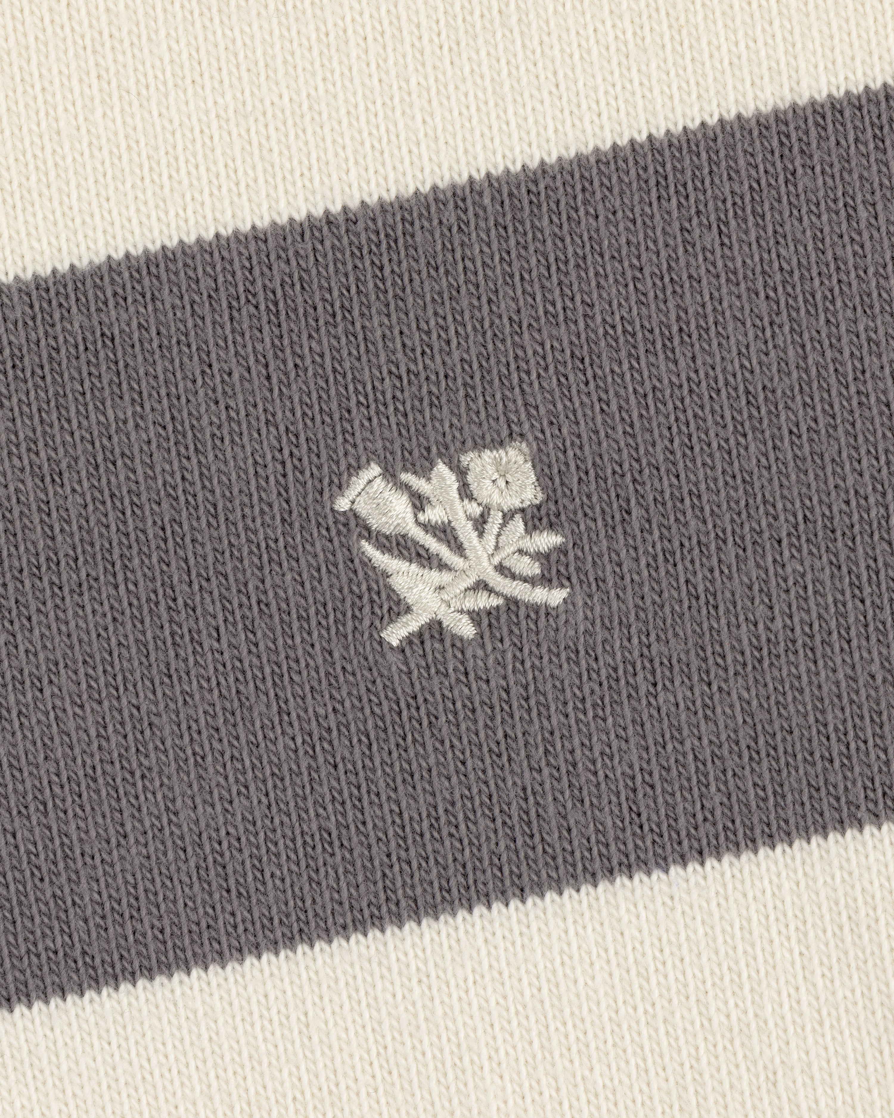 Close-up of the Striped Crest Rugby's gray and white knit fabric with an embroidered white rose emblem.