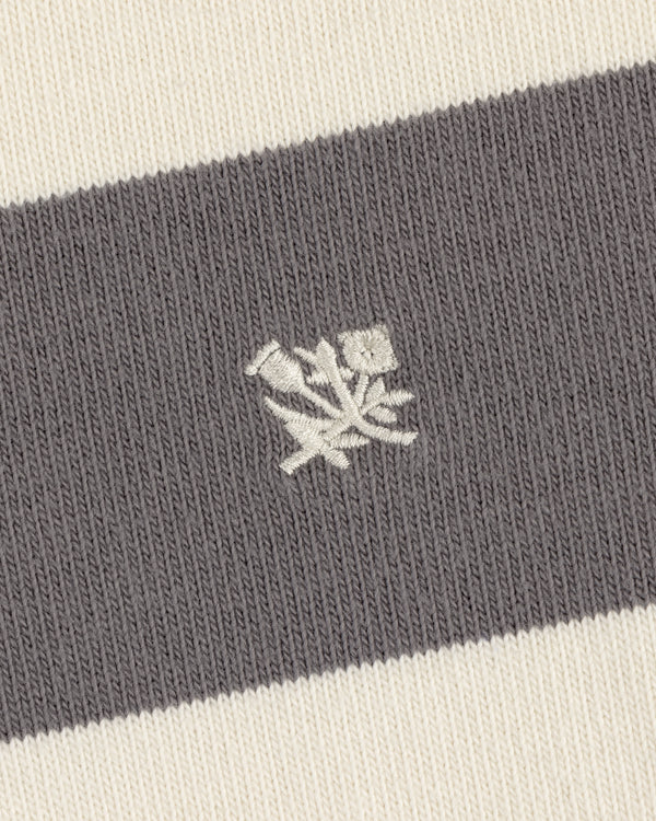 Close-up of the Striped Crest Rugby's gray and white knit fabric with an embroidered white rose emblem.