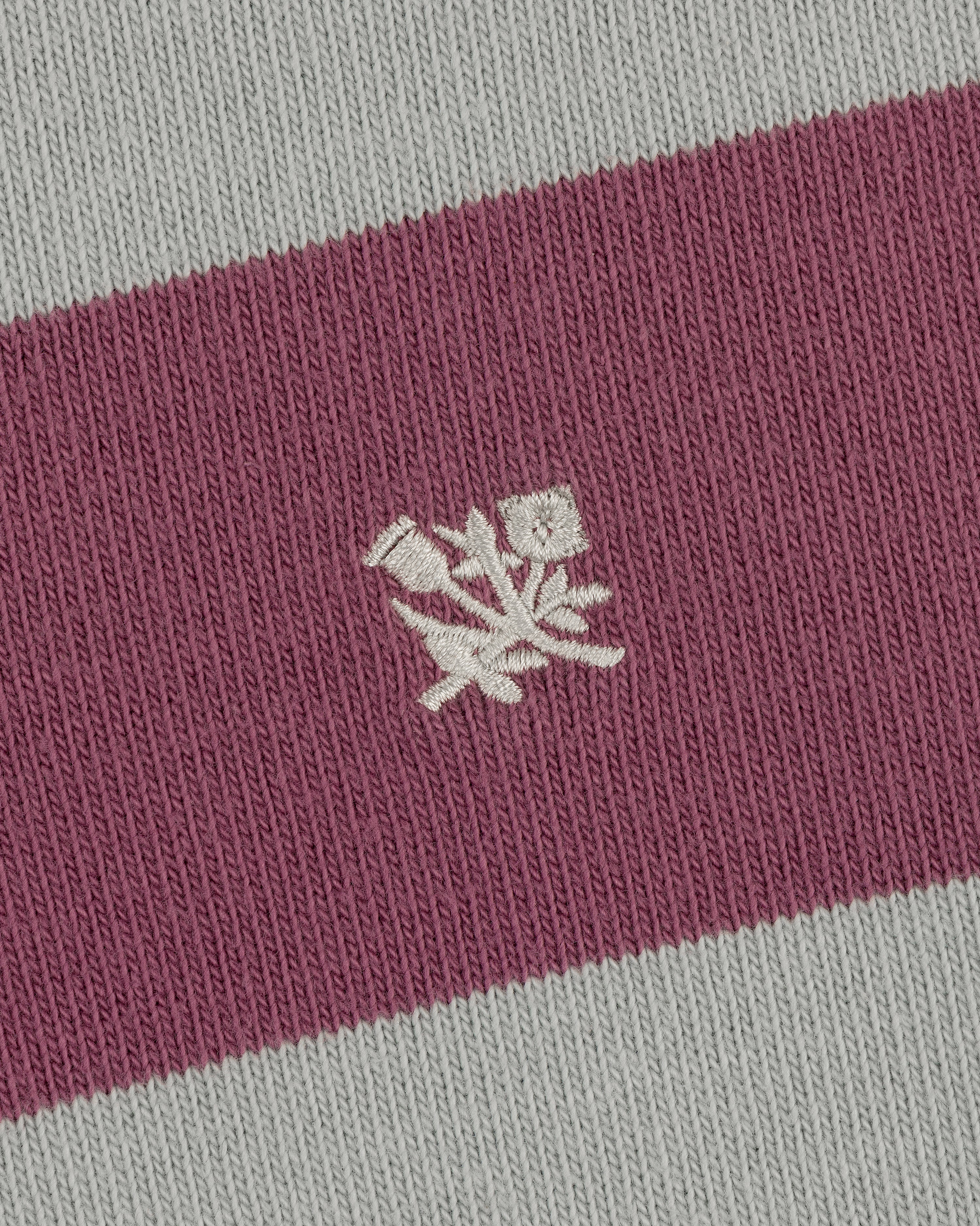 Closeup of the Striped Crest Rugby's pink and gray fabric with a small white embroidered floral design in the center.