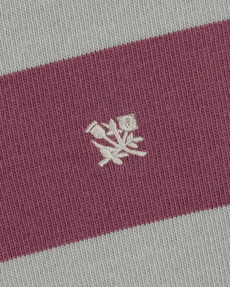 Closeup of the Striped Crest Rugby's pink and gray fabric with a small white embroidered floral design in the center.