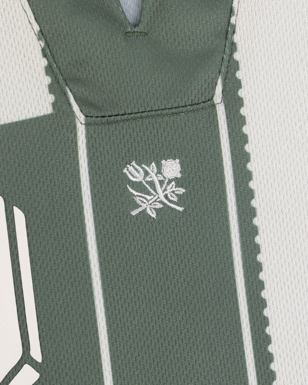 Close-up of green Aimé Cup Soccer Jersey with white stitching and two embroidered roses with stems and leaves.