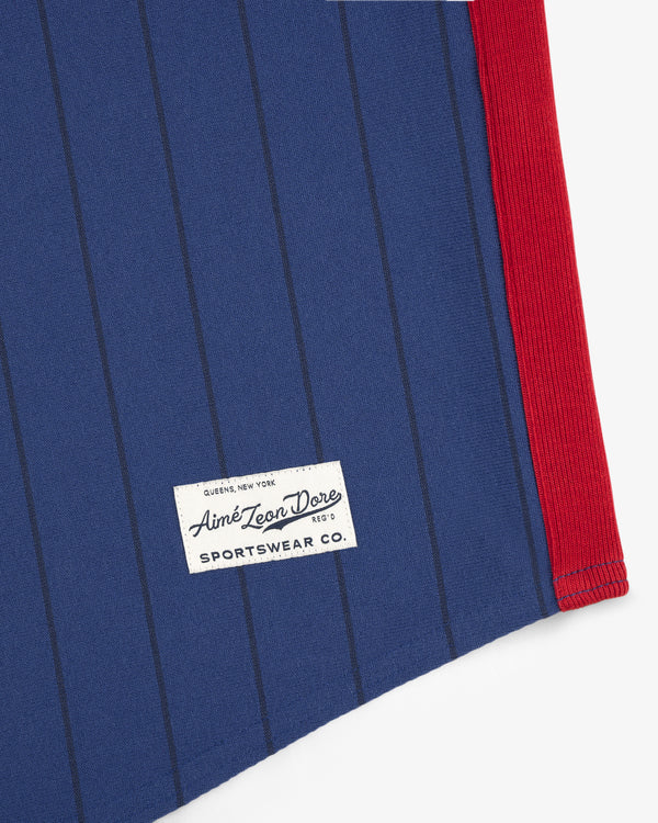Close-up of blue pinstripe fabric with red edge and white Aimé Leon Dore label on the Aimé Baseball Jersey.
